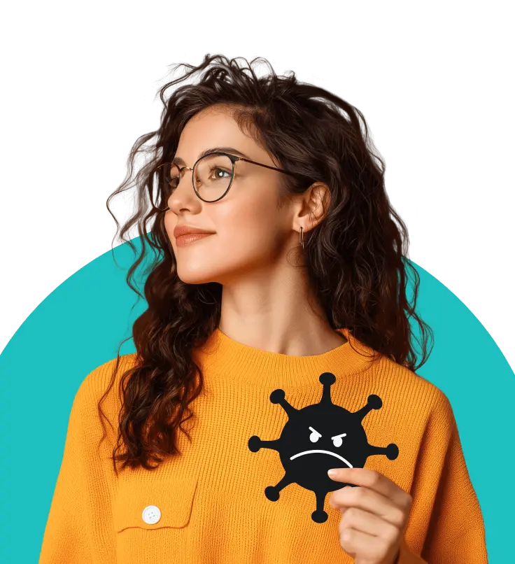 Eine Frau mit lockigem braunem Haar und Brille in einem orangefarbenen Pullover, die ein Bild eines Virus mit einem wütenden Gesicht in der Hand hält.